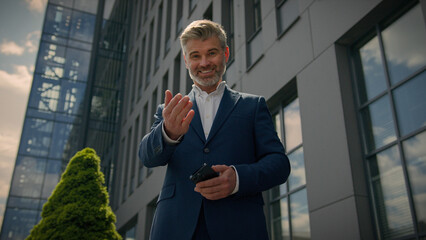 Friendly Caucasian businessman in city with smartphone invite come here gesture old senior mature business employer retired man with mobile phone showing welcome inviting interview join to job company