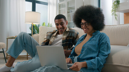 Happy husband and wife African American couple spouses family girlfriend boyfriend smiling at home man woman enjoying using laptop computer shopping online together internet buying choosing purchase