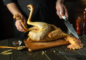 The cook preparing chicken with spices in pub kitchen. Raw broiler on a wooden cutting board. Knife...