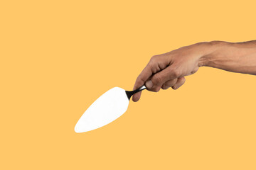 Black male hand holding a cake cutter knife isolated on yellow background