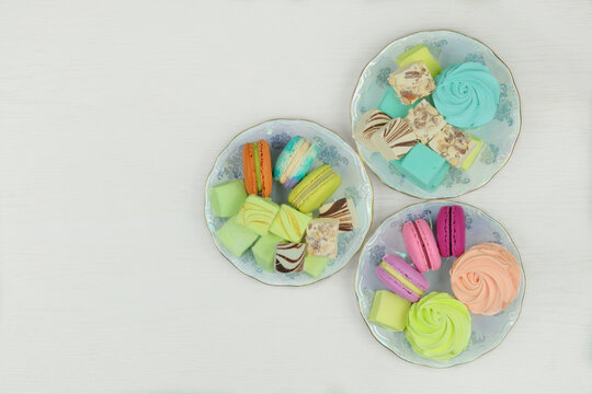 Various desserts. Sweet desserts in plates for holiday. Macaroons, marshmallows and zephyrs on a white background. Top view.