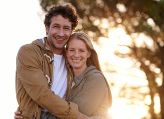 Naklejka premium Happy, couple hug and portrait in park, love and support with date for bonding and time together. Sunset, nature and people in forest for fresh air, loyalty and commitment with smile outdoor