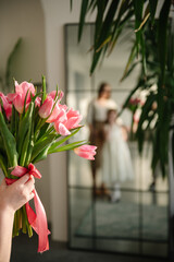 Large bouquet of pink tulips in child's hand. Mother and daughter in reflection of the mirror. Daughter hugs mom. Cute little child girl greets mother. Beautiful kid makes surprise for Mother's Day