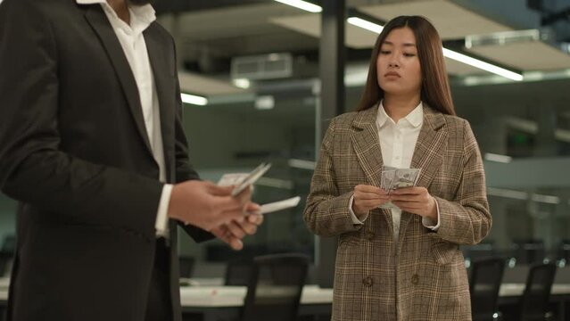 Asian sad woman worker with little salary looking at man colleague with many cash finance counting gender racial wage inequality between male female money business discrimination equal rights problem