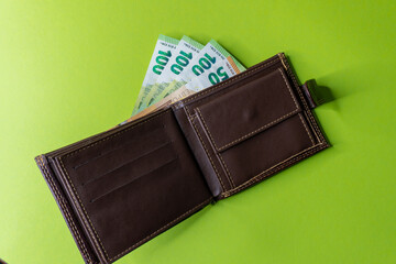 Top view of New brown genuine leather wallet with banknotes and credit card inside isolated on orange background