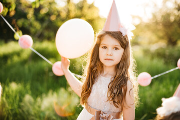 Happy birthday little girl making wish blowing candles on cake with pink decor in beautiful garden. 4 years birthday. child eat happy birthday pink cupcake. colorful pastel decoration outdoor - 756410751