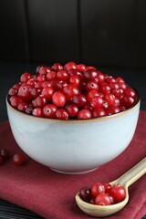 Cranberries in bowl and spoon on black wooden table, closeup