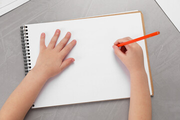 Little boy drawing with pencil at grey textured table, top view. Child`s art