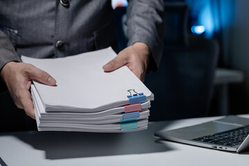 An employee was tidying up a pile of documents piled on his desk before returning home from work, A businessman is tidying up his desk because there are many documents he has completed.