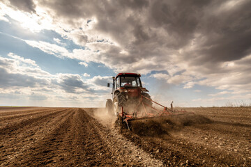 Agricultural scene of a tractor plowing dry soil, kicking up dust with a dramatic sky overhead