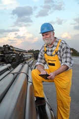 Smiling worker with tablet in hands and heap of insulated pipes for natural gas