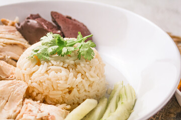 Hainanese chicken rice with coriander, cucumber and chicken soup on black background. Local food in East and Southeast Asia