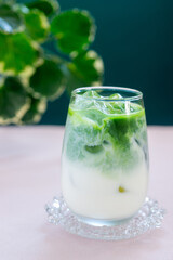a glass of ice matcha latte on pink table.
