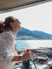 Beautiful blond woman sailing on a yacht in the Mediterranean Sea operating the winch to adjust the sails