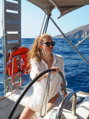 Beautiful blond female skipper at the helm sailing on a yacht in the Mediterranean Sea