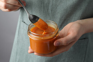 Woman with delicious persimmon jam on gray background, closeup