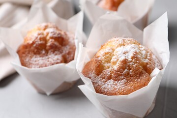 Delicious muffins with powdered sugar on light table, closeup