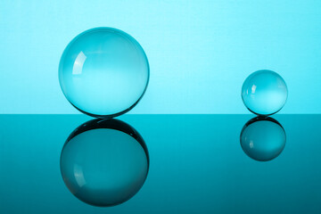 Transparent glass balls on mirror surface against turquoise background