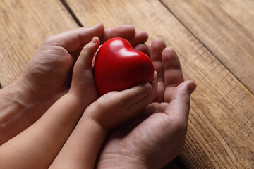 Father and his child holding red decorative heart at wooden table, closeup