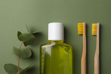Fresh mouthwash in bottle, toothbrushes and eucalyptus branch on green background, flat lay