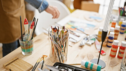 Man artist's hands gripping paintbrush, standing engrossed in painting canvas in well-attended art...