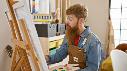 Handsome, focused redhead young man channeling his creativity, drawing art in the studio,...