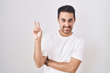 Handsome hispanic man standing over white background smiling with happy face winking at the camera...