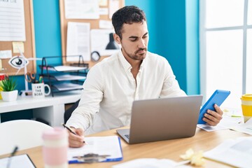 Young hispanic man business worker using touchpad writing on document at office