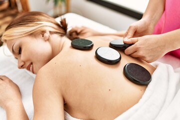 Obraz na płótnie Canvas Young caucasian woman lying on table having back massage using hot stones at beauty salon