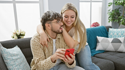 A loving couple enjoys time together indoors, with the woman showing something on a smartphone to...
