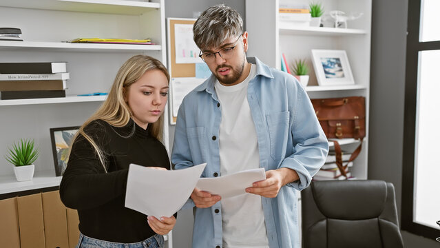 A focused man and woman evaluate documents together in a modern office setting, showcasing teamwork.
