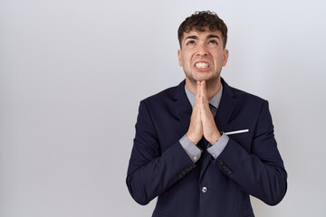 Young hispanic business man wearing suit and tie begging and praying with hands together with hope...