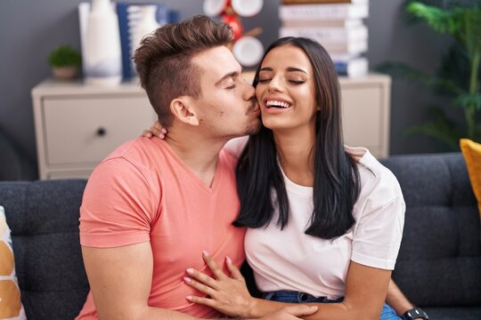 Man and woman couple hugging each other and kissing sitting on sofa at home