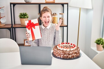 Joyful young blonde woman celebrating birthday victory on a video call at home. winner expression, confident smile with a gift. cheers to her successful achievement!