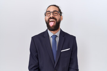 Hispanic man with beard wearing suit and tie sticking tongue out happy with funny expression....
