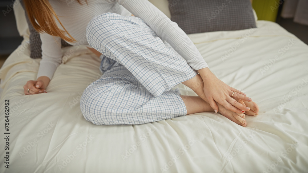 Wall mural a young caucasian woman in pajamas stretches on a bed in a cozy bedroom, showcasing a relaxed lifest