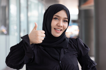 Smiling Muslim Woman Expressing Agreement with Thumb Up Gesture and looking at you, concept image of Encouragement, Support, Agreement, Satisfaction, Acceptance, Approval, Consent, Positive expression