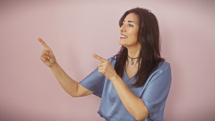 Hispanic woman in blue pointing upwards on pink background
