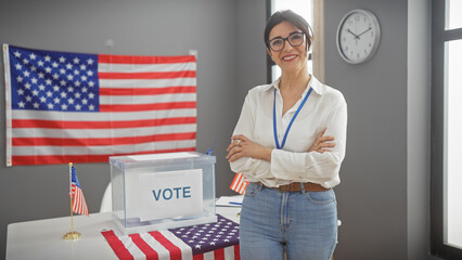 Hispanic mature woman with crossed arms smiling confidently in a united states voting center with...