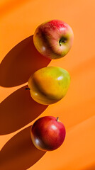 Two vibrant red apples and a mango cast long shadows against an orange backdrop, creating a fresh and modern aesthetic. Ideal for health and wellness themes. 