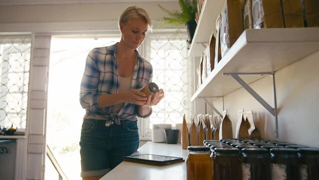 Mature Woman Working In Sustainable Plastic Free Store Checks Stock With Digital Tablet And Stylus