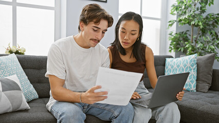 Interracial couple reviews documents together in a well-lit living room with modern decor.