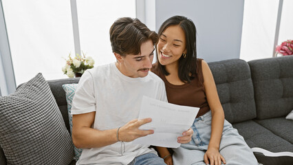Interracial couple reviews documents in cozy apartment living room, embodying unity and partnership.