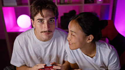 Interracial couple enjoying a gaming session together in a modern, colorful room at night.