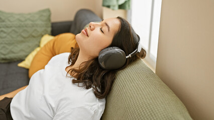 Young hispanic woman relaxing with headphones on a couch in a cozy living room