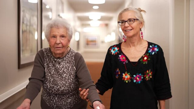 Senior elderly old mother using a walker and daughter in law walking to elevator in senior living home during a family visit.