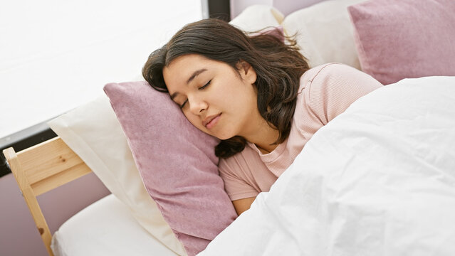 A young hispanic woman sleeps peacefully in a well-lit, cozy bedroom setting, embodying tranquility and comfort.