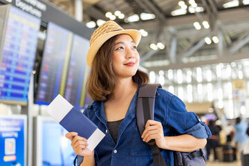 Young Asian woman passenger with her carry on luggage is looking at her boarding pass after self...
