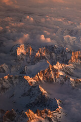 Fototapeta premium Sunset over Italian Alps. Aerial vertical photo with the amazing mountain peaks covered with snow from Alps Mountains and sea of clouds between them. Nature landscape with mountains in sunset light.