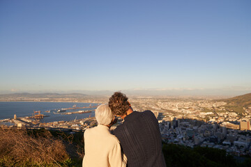 Senior, couple and city skyline outdoor, happy elderly people on hill for scenic view of buildings and sky. Bonding, care and affection at sunset, hugging and love and relationship or panorama